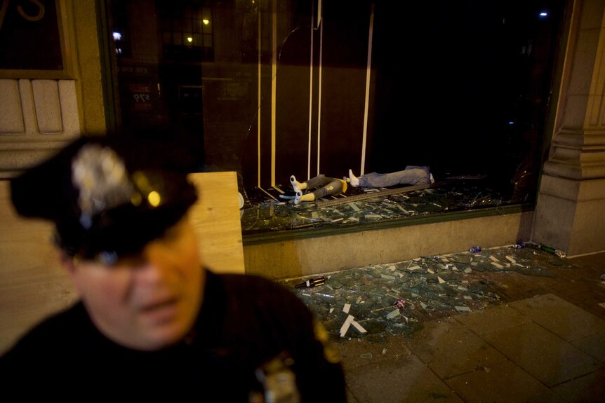 A police officer stands beside a destroyed Macy's storefront window.