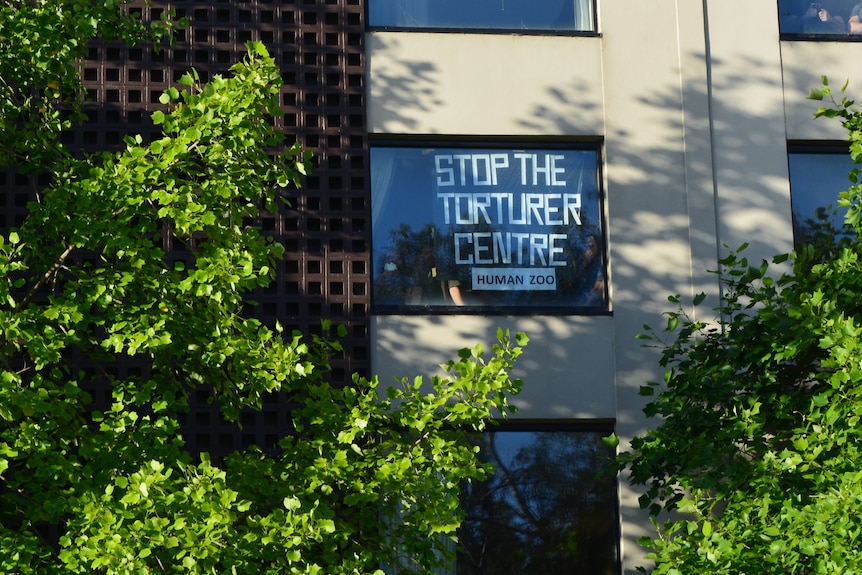 A sign in a window reads: 'Stop the torturer centre'.