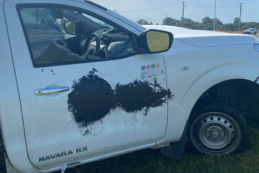 A white ute with its window smashed and other markings on its side. 