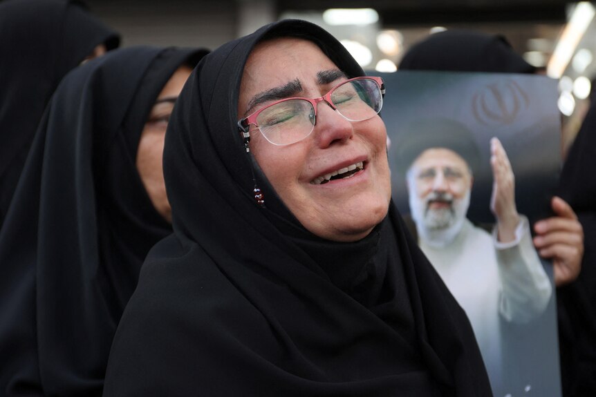 A women wearing a black hijab and glasses with her eyes closed in a crying manner