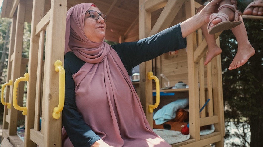 a woman in a headscarf sitting in a cubby house looking at a child