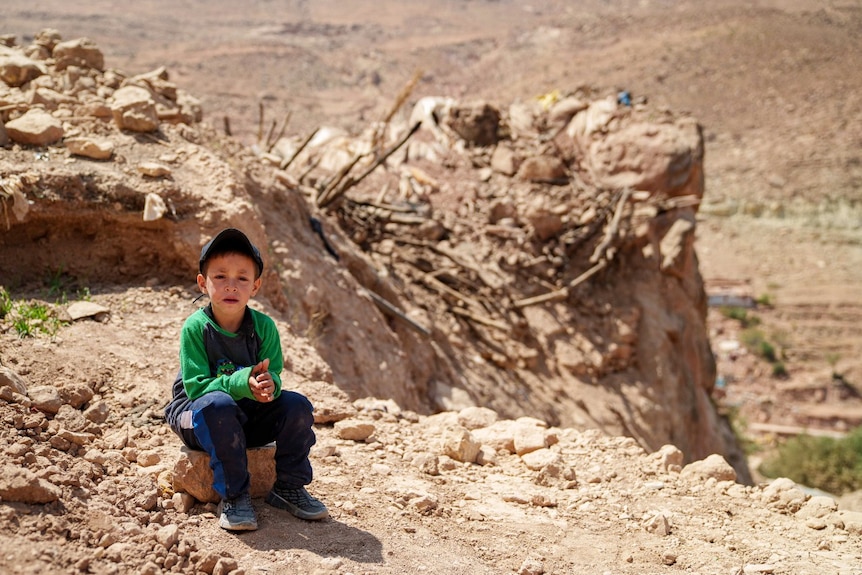 A young boy, crying, sits on a rock.