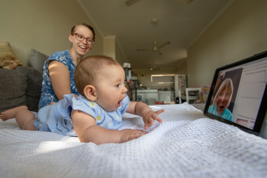 A baby girl reaches toward her grandma, who appears on an iPad screen.