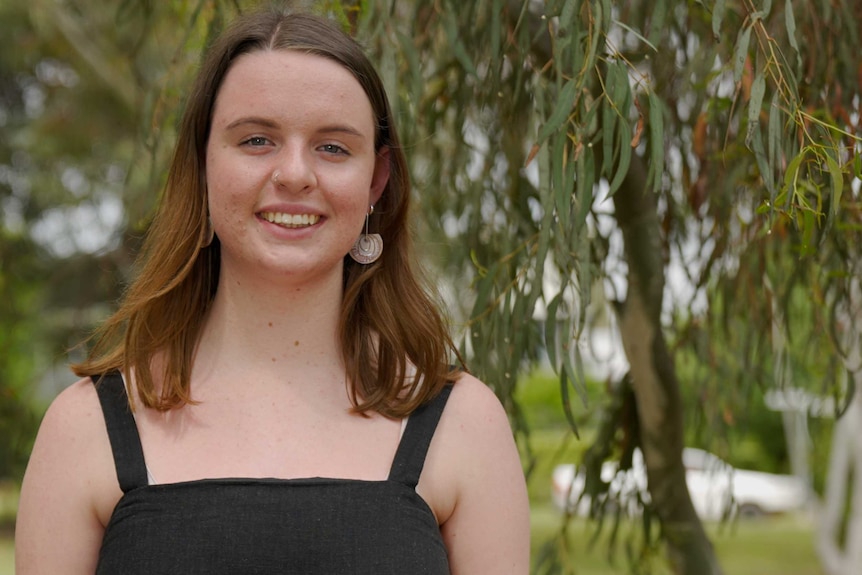 A young woman stands under a tree smiling