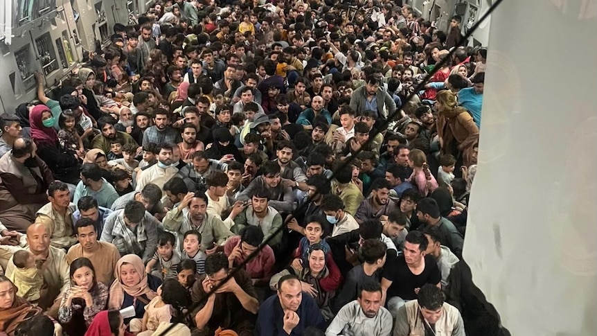 A crowd of people is tightly packed inside a large military plane.