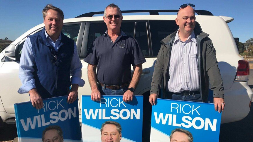 Three Liberal supporters holding up campaign posters.