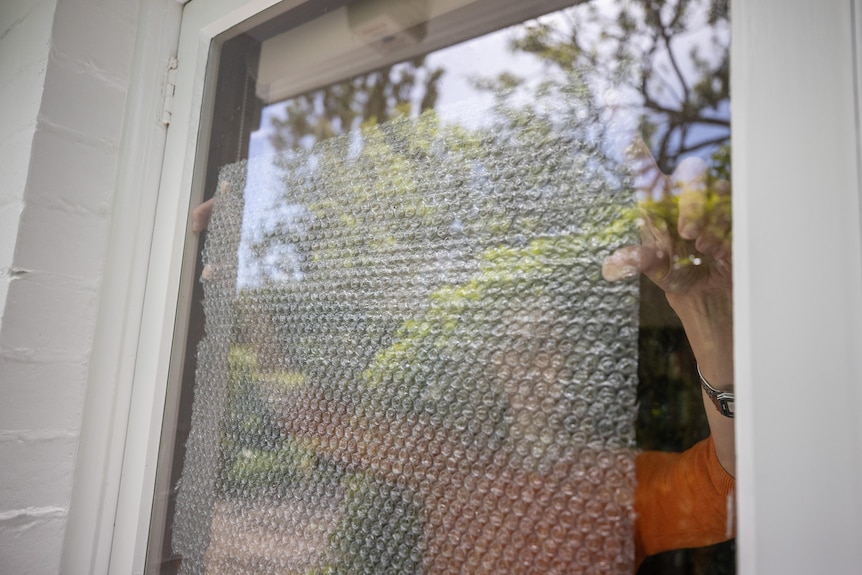 A woman spreads bubble wrap on a window.