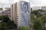 Very tall mural of a young woman on apartment block.