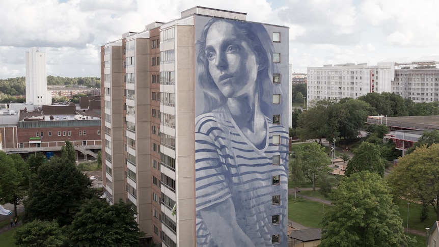 Very tall mural of a young woman on apartment block.