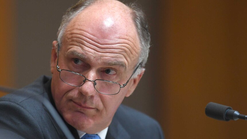 Eric Abetz, with glasses lowered, looks over his shoulder during Senate estimates.