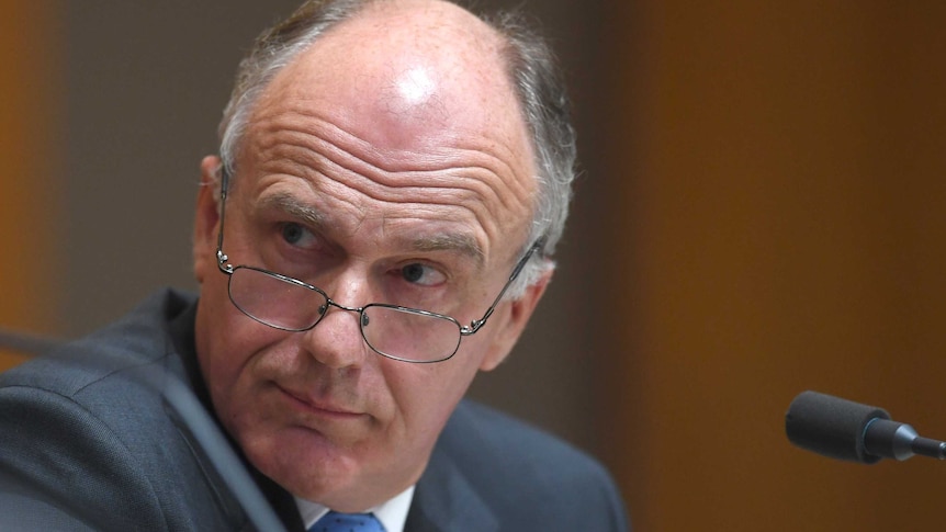 Eric Abetz, with glasses lowers, looks over his shoulder during Senate estimates.