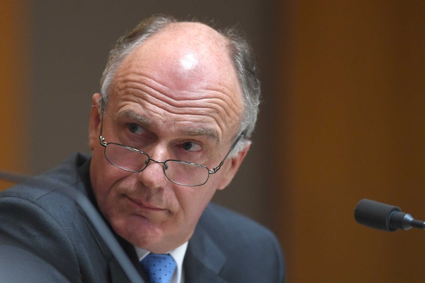 Eric Abetz, with glasses lowers, looks over his shoulder during Senate estimates.