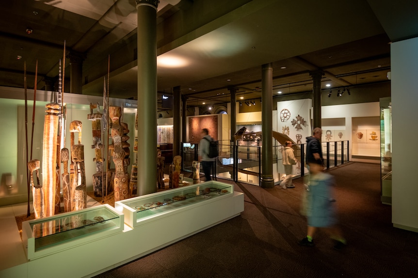 People walking among museum exhibits and artefacts, some enclosed in glass cabinets