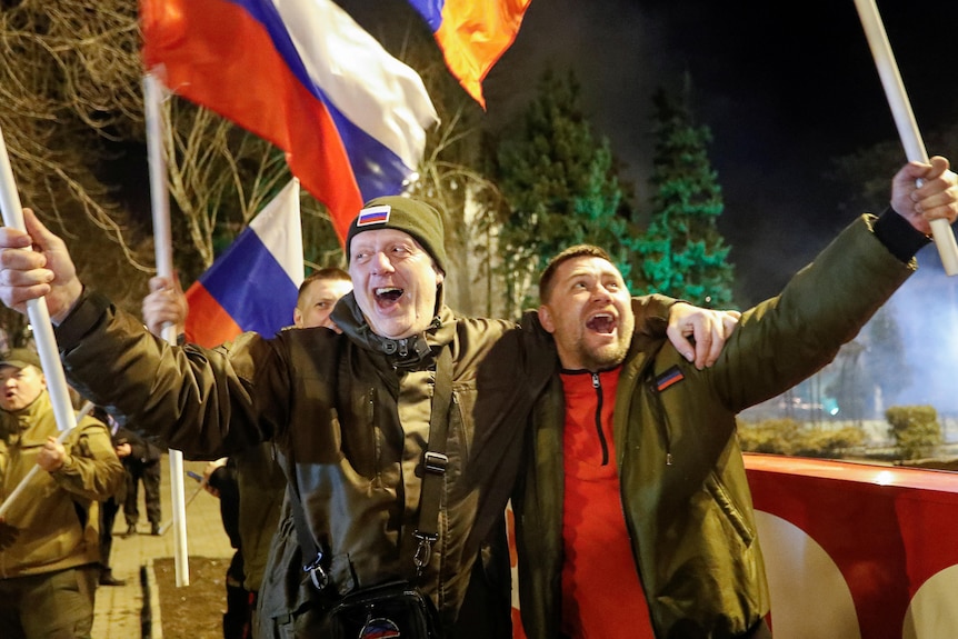 Two men holding Russian flags smile in the street.
