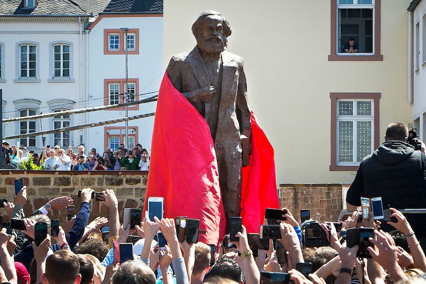 A red sheet is removed to reveal a bronze statue of German philosopher Karl Marx