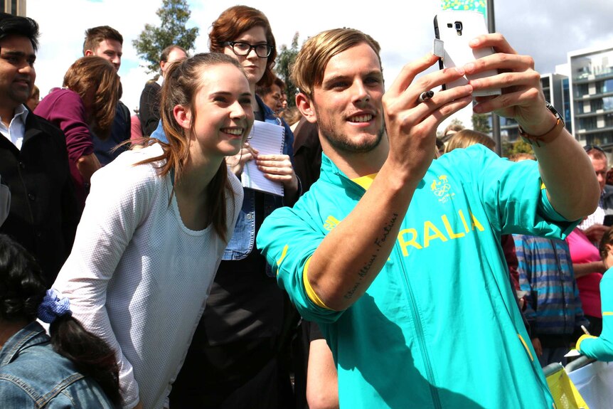 Kyle Chalmers holds up a phone to take a selfie with a fan