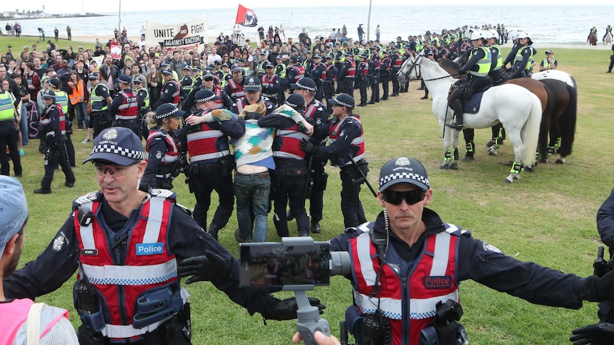 Police keep protesters apart as a man is arrested on the St Kilda foreshore in Melbourne