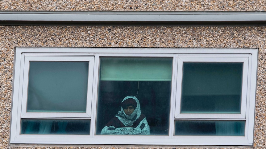 A woman looks out a window from a locked-down public housing tower in Melbourne.