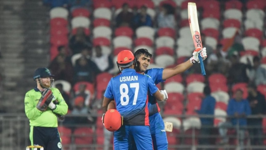 Hazratullah Zazai raises his bat in his left hand whilst being hugged by a teammate