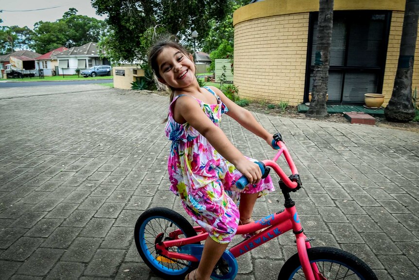 Karla De Lautour wears a huge grin while she rides her bike on the driveway outside her house.