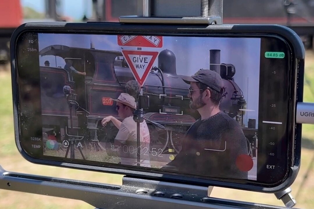The view through an iphone camera to two men filming a steam train as it passes by