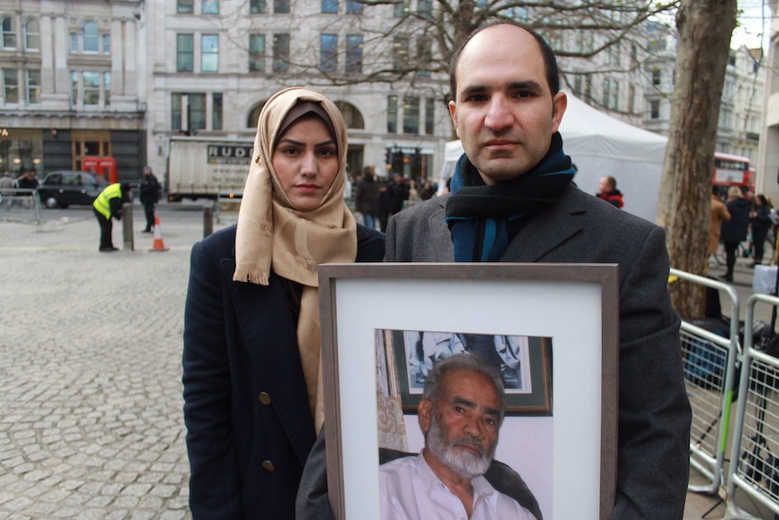 A man holds a photo of his father while standing next to his wife.