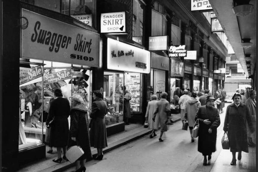 Black and white photo of women walking down a laneway filled with clothing stores.