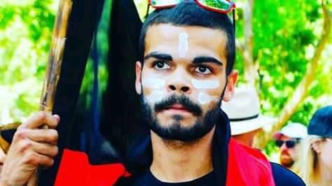 A man, with an Indigenous flag draped around his shoulders, and painted face