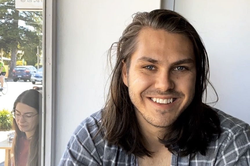 Ethan Taylor has hair down to his shoulders and is smiling at the camera.