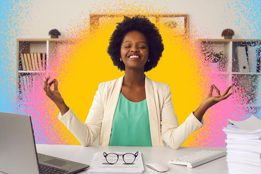 A woman sitting at a desk smiles while holding her fingers as if she's meditating.