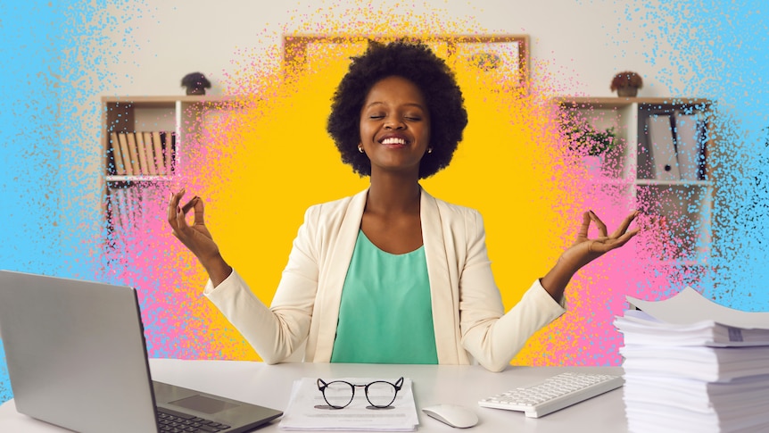 A woman sitting at a desk smiles while holding her fingers as if she's meditating.