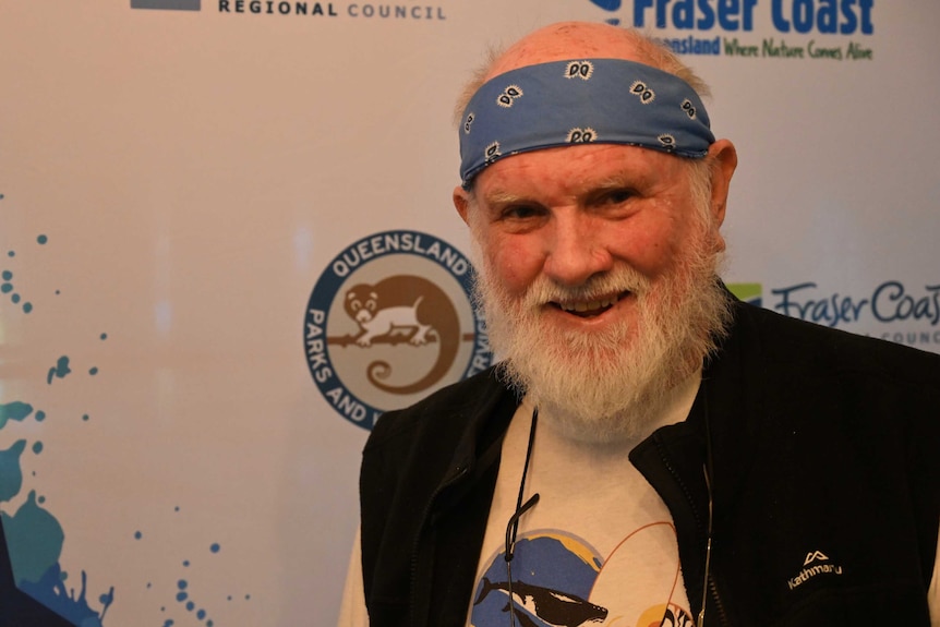 A whale researcher in a bandana smiles in front of a tourism sign in Hervey Bay in early October, 2019.