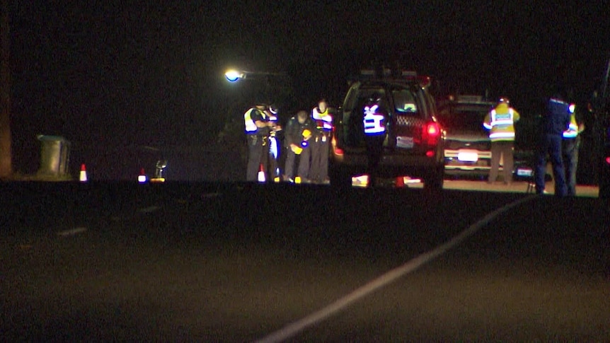 Police officers stand around on a road looking at the scene of a crash