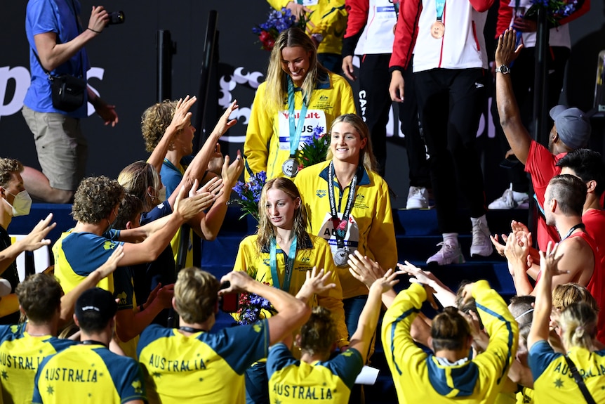 An Australian women's medley relay team walks around the pool after receiving medals at the world titles as teammates cheer. 
