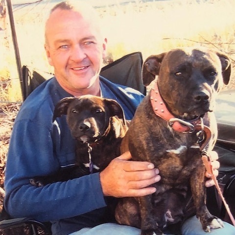 A man smiles at the camera with two dogs on his lap
