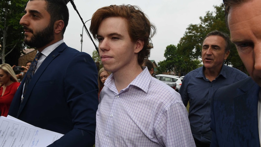 A man in a checked shirt is flanked by several people