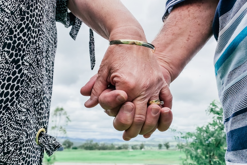 A close up on an older couple holding hands.