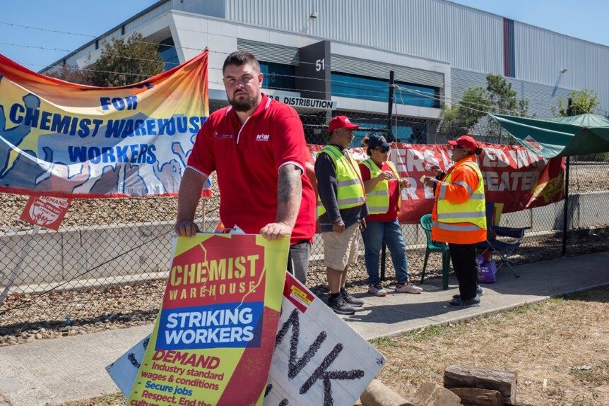 Dave Hiah stands in front of a sign reading 'striking workers'.