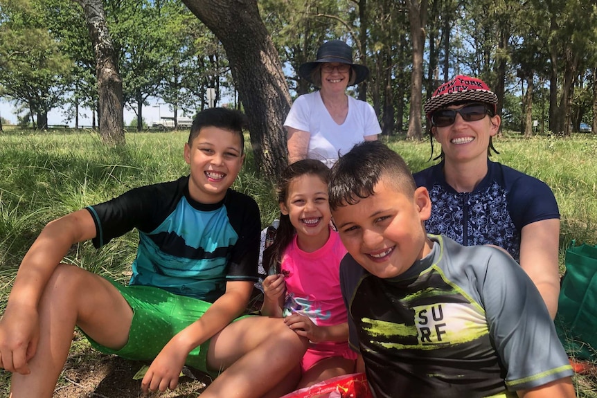 A family sits on grass, wearing swimmers, smiling at the camera