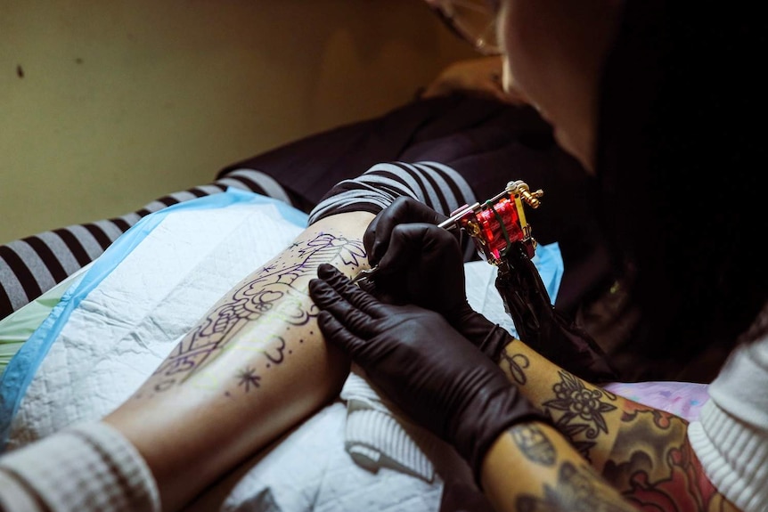 A female tattoo artist, Mimsy Gleeson, works out of a pop up studio, tattooing a woman's leg