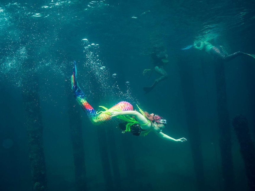 A woman with brightly coloured mermaid tail swimming underwater