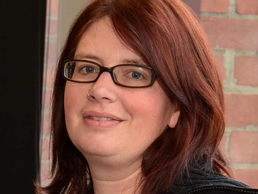 A portrait photo of a young woman with brown hair wearing glasses and smiling.