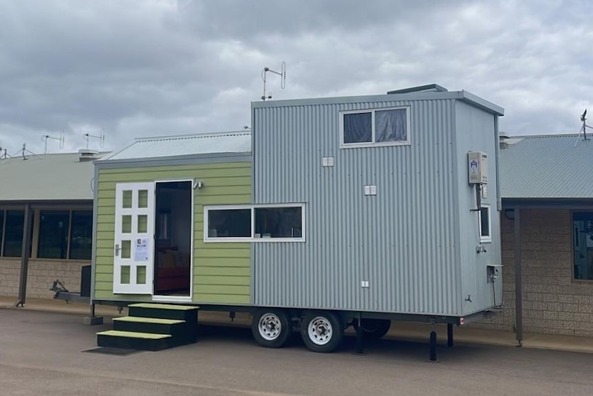The tiny house has wheels and is green and corrugated iron