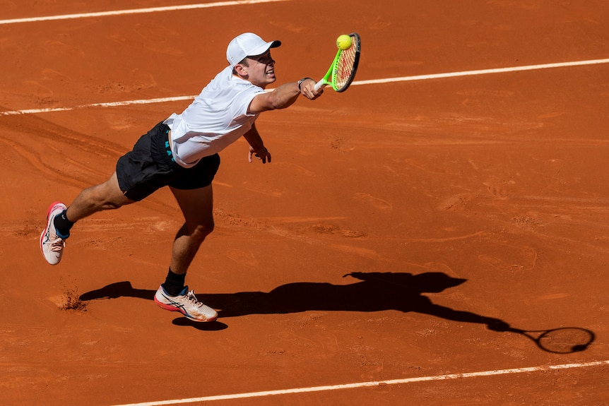 Alex de Minaur stretches to play a back hand on red clay.