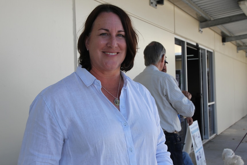 Woman with short brown hair wearing a white button up shirt smiling at the camera.