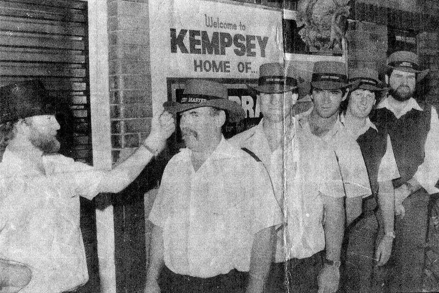 Five male rail workers in a line wearing akubra hats, with an Akubra worker checking their hats. 