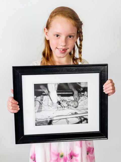 Jesse holds a black and white photo of a baby with a lot of tubes connected to her.