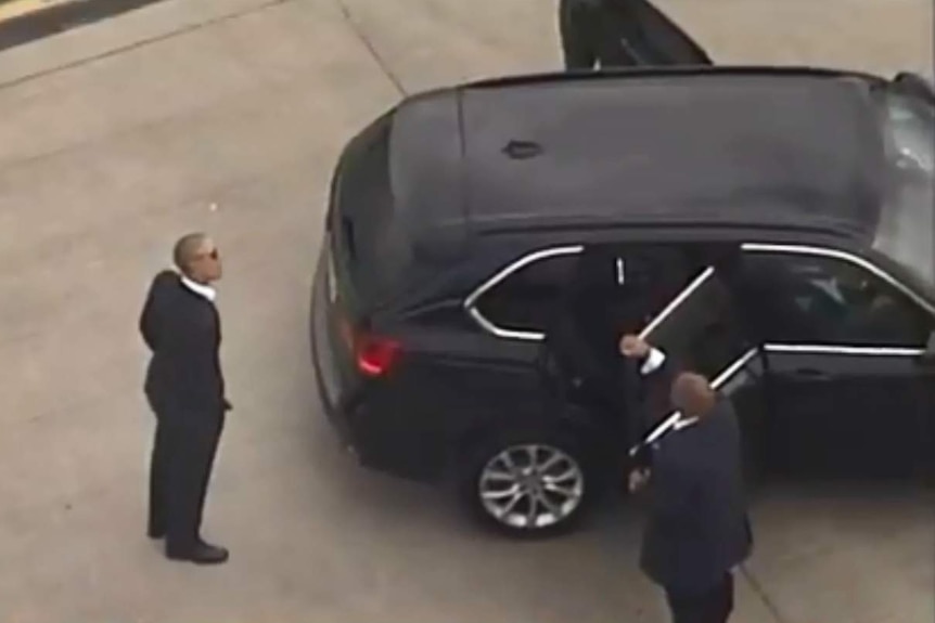 A man stands near a large black car.