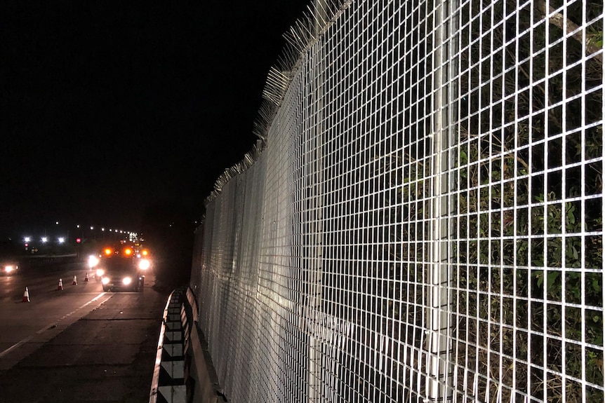 Mesh fence beside highway at night.