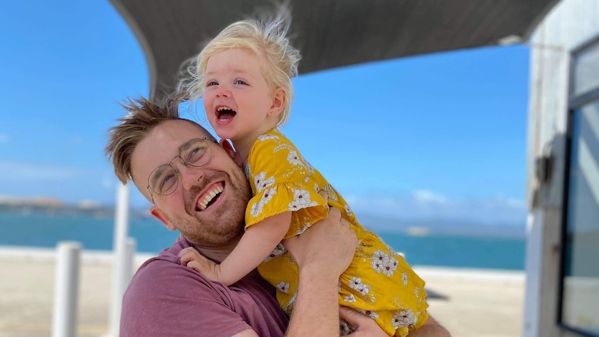 Man smiling at camera with his arms around a little girl